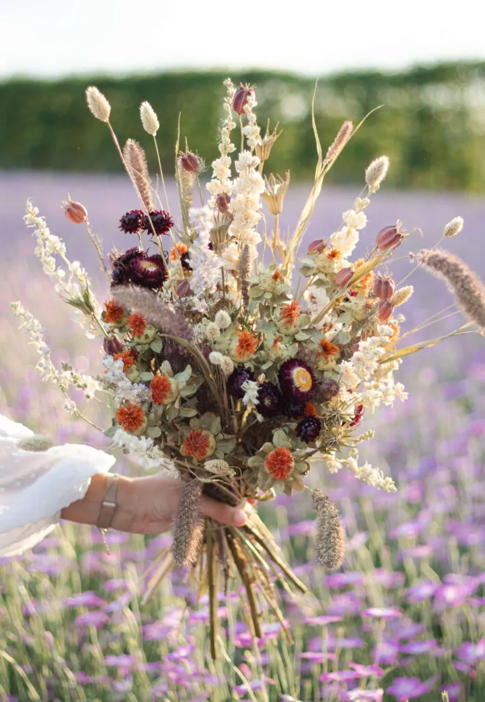 Handgebonden boeket met roze en witte bloemen, vastgehouden in een lavendelveld